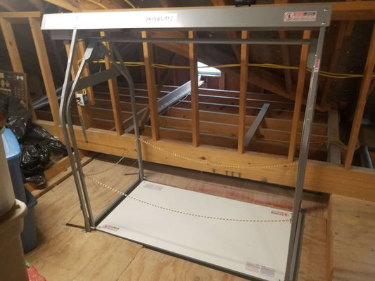 A VersaLift attic storage lift installed between joists in an unfinished attic space.